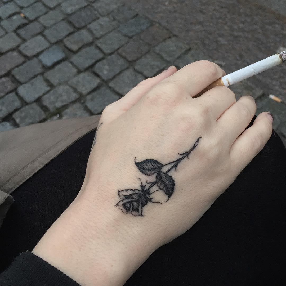 a small black rose tattoo on hand